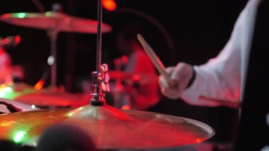 Adam sahnedeki bando eşliğinde bagetleriyle metal zillere vuruyor. Genç davulcu gece kulübü partisinde ritmik müzik çalıyor.