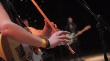 Gitarist sahnede mikrofon rafının yanındaki flütte solo çalıyor. Müzisyen, gece kulübünde bando eşliğinde canlı performans sergiliyor.