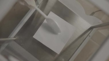 Assistant pours white powder on paper with spoon in laboratory closeup. Using dry substance for scientific research in chemical lab