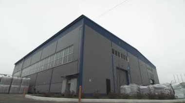 Warehouse building and pallets with packaged products in yard under cloudy sky. Industrial storage of production plant on gloomy day