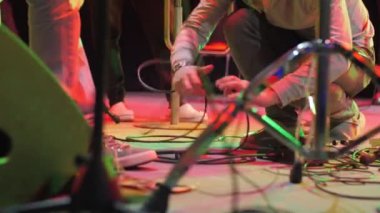 ALMATY, KAZAKHSTAN - NOVEMBER 28 2023: Assistant on large stage untangles necessary equipment with specific wire to connect and switch on electric guitar of artist. Concert preparations