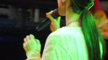 ALMATY, KAZAKHSTAN - NOVEMBER 28 2023: Lady finishes last song of band at rehearsal announcing that preparations complete. Vocal performer listens to band play on stage singing along