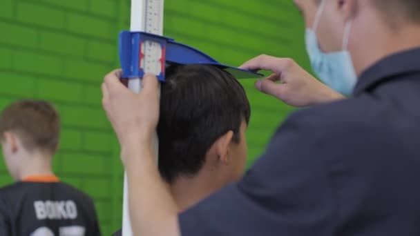 Man Coach Medical Mask Measures Child Height Closeup Future Athletes — Stock Video