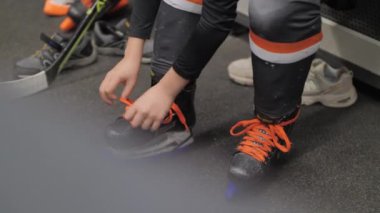 Child tightens laces on skates boots before hockey training. Boy getting ready to start practicing on ice wearing professional footwear