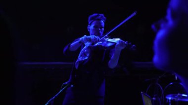 ALMATY, KAZAKHSTAN - NOVEMBER 28 2023: Man with violin enthusiastically plays energy music for guests on stage in nightclub. Musician engages in playing string instrument on stage