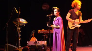 ALMATY, KAZAKHSTAN - 28 Kasım 2023: Gece elbisesi giymiş kadın şarkıcı sahnede gitaristle birlikte şarkı söylüyor. Konser salonundaki müzik severler için duygusal caz gösterisi