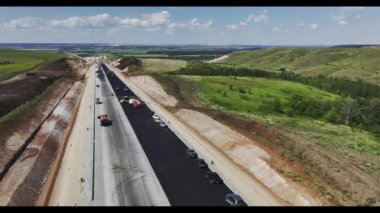 Modern makineler yaz kırsalında otoyol şeridinde yeni asfalt döşüyorlar. Yeşil vadi boyunca geniş otoban manzaralı.