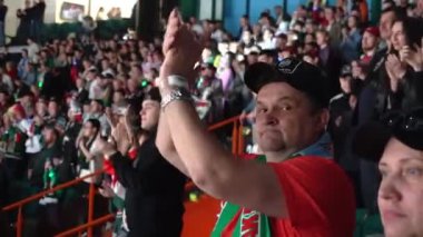 ALMATY, KAZAKHSTAN - 22 Aralık 2023: Sevgi dolu takım eşarplı olgun adam oyunculara destek veren ellerini çırpıyor. Hokey arenasındaki Tribün maç bekleyen hayranlarla dolu.