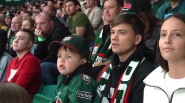 ALMATY, KAZAKHSTAN - 22 Aralık 2023: küçük çocuk sevgili takımı desteklemek için bağırıyor. Anaokulu erkek hokey takımı maç boyunca Tribün 'de diğer taraftarların arasında oturup babalarının kucağına oturdu.