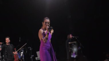 ALMATY, KAZAKHSTAN - NOVEMBER 29 2024: Kadın vokalist, grup üyeleriyle sahnede duran seyirciyle popüler bir şarkı söylüyor. Müzisyenler, unutulmaz deneyimler sağlayan hayranları eğlendiriyor