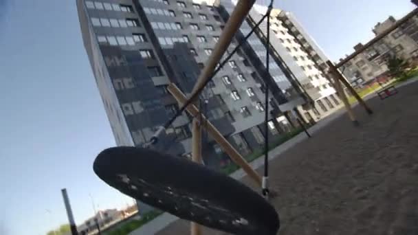 サーキュラースイングは 都市の建物の近くの遊び場で風で激しく振動します スイングの背景にある建築近代都市の建物 — ストック動画