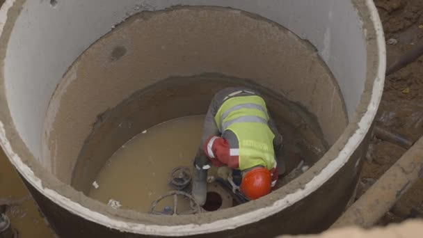 アルマニー Kazakhstan August 2023 コンクリートでパイプラインをしっかり留める安全ベストねじのプラム 労働者は開いたマンホールの内部に立っている壊れた下水管を修理します — ストック動画