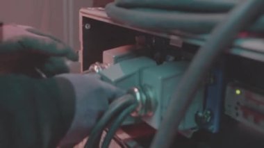 Koruyucu eldivenli işçiler elektrik kablosu takıyor sahne ekipmanlarını kapatıyor. Elektrikçi stüdyodaki kabloları panele çeviriyor.