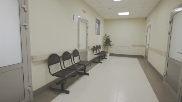患者の快適な待機のために椅子が付いている病院回廊 広々としたクリニックの空の廊下と植物で装飾された井戸 — ストック動画