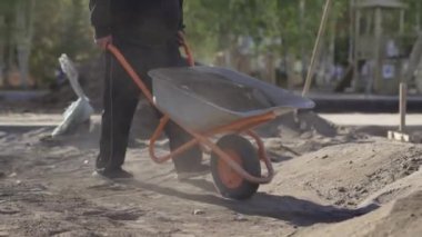 Üniformalı bir erkek işçi inşaat alanındaki el arabasından kum boşaltıyor. Kentsel inşaat sahasında günlük iş akışının bir parçası