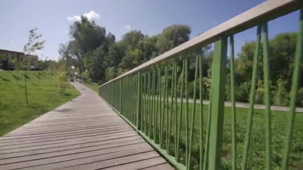 市立公園の緑に囲まれた手すり付きの木製ボードウォーク 近代的なレクリエーションエリアは訪問者のための穏やかな環境を提供します — ストック動画