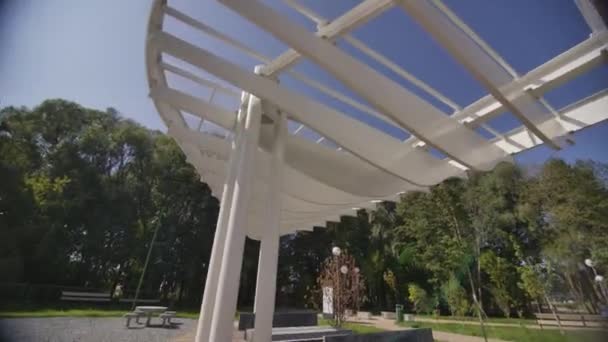 市立公園でリラックスするためのユニークなデザインのホワイトガゼボ 特別な革新的な構造は夏の日に住民に日陰を提供します — ストック動画