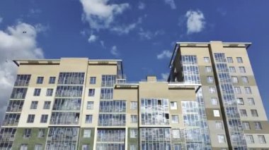 Gökyüzüne bakan panoramik pencereli, bulutlu, yüksek bir bina. Parlak parlak gökdelen camları güneş ışığını yansıtır.