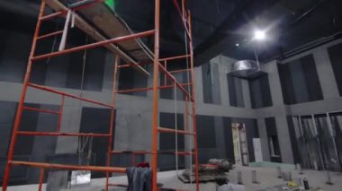 Büyük bir ticari binanın restore edilmiş koridorunda yüksek metal iskeleler var. Oda içi bakım için çalışan ekipmanlar. Yeniden yapılanma süreci