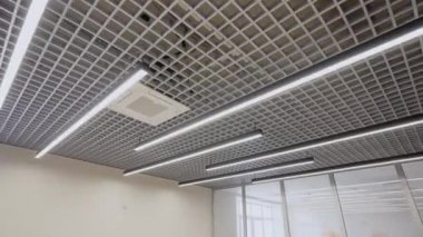 Tavanı modern uzun lambalarla süslenmiş ofis odası. Temiz çizgiler ve minimalist tasarım odaya çağdaş zarafet katar.