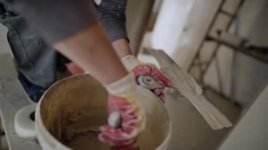 Kadın işçi, duvarları tamamlamak için kovadan spatulayla sıva topluyor. Eldivenlerdeki yetenekli kadın tadilat yapıyor.