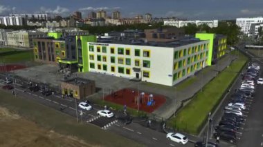 Okulun girişine giden öğrencilerle dolu bir yer. Modern okul binası kaldırımlar ve iyi organize edilmiş park yerleriyle çevrili.