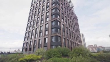 Yeşil çimenli arsa ve yüksek konut binasının yakınındaki ağaçlar. Modern ofis binası bulutlu gökyüzüne uzanan alçak açılı çekim