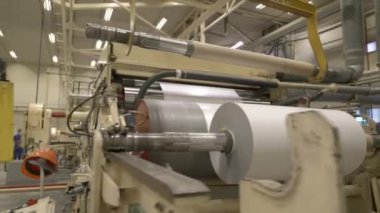 ALMATY, KAZAKHSTAN - 12 Temmuz 2024: İşçi atölyede dönen metal varillerle kağıt pres makinesini kontrol etmek için yürür. Kağıt fabrikasında selüloz madde işleme makineleri