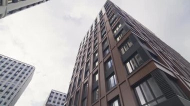 Bulutlu gökyüzüne karşı modern apartman ve ofis binaları. Şehir caddesinde yerleşim yerleri var. Düşük açı, yuvarlak hareket.
