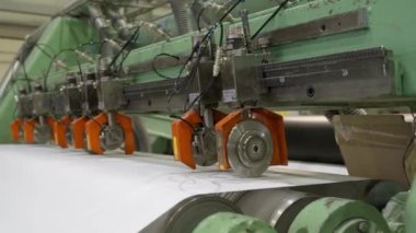 Metal silindirler, fabrika atölyesindeki üretim hattında basın kâğıdına sarılıyor. Makine aracı fabrikada uzun malzeme şeridi taşır