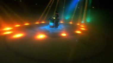 ALMATY, KAZAKHSTAN - 21 Şubat 2024: Enerjik DJ renkli ışıklar altında coşkulu bir şekilde sahnede çalıyor. Dijital oynatıcıyla bekletme konserinin bir kısmı gösteriliyor