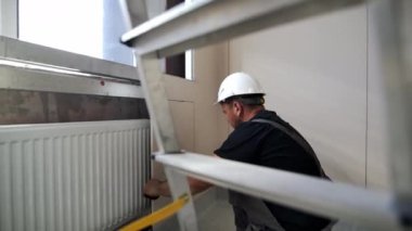 ALMATY, KAZAKHSTAN - 15 Mart 2024: İnşaatçı duvara yonga paneli takmaya hazırlanıyor. İnşaat işçisi, güvenli eklenti sağlamak için vidaları yonga paneline sokar