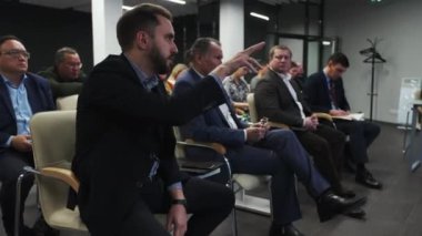 ALMATY, KAZAKHSTAN - 22 HAZİRAN 2024: Dinleyiciler grubundan koyu renk ceketli bir adam konuşmacı ile konuşuyor. Ciddi bir adam sunumu işaret ederek materyal hakkındaki düşüncelerini ifade eder
