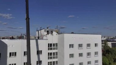 Endüstriyel tırmanışçılar binanın ön cephesini çatıdan boyuyorlar. Güvenlik kemeri takan işçiler duvarları boyama sürecinde binanın çatısından sarkıyorlar.