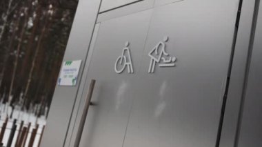 Engelli insanlar için tuvalet ve şehir parkında çocuklu bir anne. Sokak tuvaletinin kapısındaki bilgi tabelaları. Kentsel alandaki kolaylıklar