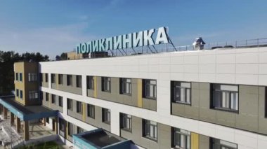 Klinik ön cephesinde çatıdan bakıldığında kocaman, şehvetli harflerden oluşan bir tabela var. Koyu plastik çerçevelerle süslenmiş pencereler güneş ışığını yansıtır