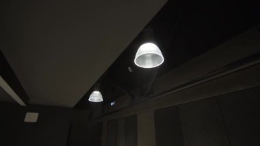 Otel odasının tavanına asılmış modern lambalar yumuşak bir şekilde parıldıyor. Loş ışıklandırma davetkar atmosfer yaratarak misafirler için konforlu konaklama sağlıyor