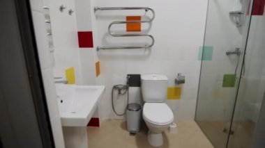 Duvarlarında çok renkli seramik fayanslar olan temiz bir banyo. Banyo içi duş kabini, tuvalet ve aynalı otel. Ev dekorasyonu