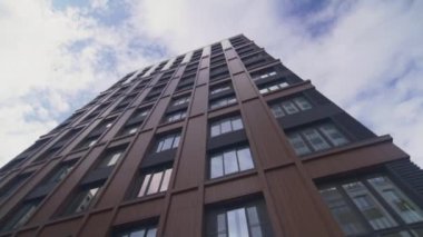 Şehir merkezinde büyük pencereli bir ticari bina var. İş alanındaki ofis binasında, bulutlu gökyüzü alçak açılı çekime karşı modern cephe yer alıyor