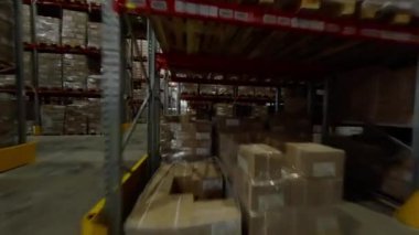 Deponun içi karton kutularla dolu uzun metal raflarla dolu. Raflar arasındaki geniş koridorlar forkliftlerin malları kolayca taşımasına olanak sağlar