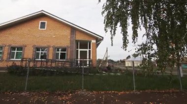 Yeşil banliyö bölgesinde koyu tahta çatılı tuğla bina. Köy binasının geniş pencereleri bulutlu gökyüzünü yansıtır. Sıcak sonbahar atmosferi yaratır.