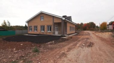 Tekerlekli sandalye rampası olan tuğla bina toprak yolun yanında duruyor. İnşaat çalışmalarının devam ettiğini gösteren yeni yapılmış toprakla çevrili bir bina.