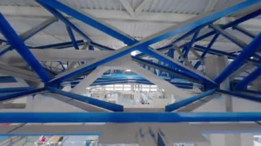 Büyük bir kağıt ve mukavva fabrikasının metal çatı yapıları. Uzun kirişler çatı ve lambaları destekliyor. Yerdeki kutularla depoyu aydınlatıyor.