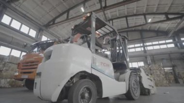 ALMATY, KAZAKHSTAN - 24 Eylül 2024: Sürücü tarafından yönlendirilen mekanize forklift atık kağıt balyalarını taşıyıcıya dağıtıyor. İşlem için ham madde taşımacılığı