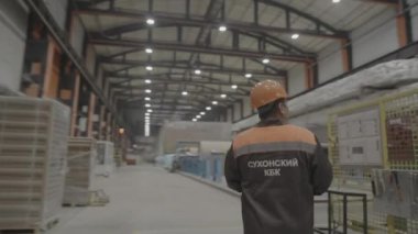 ALMATY, KAZAKHSTAN - 24 Eylül 2024: Üniformalı ve miğferli fabrika çalışanı otomatikleştirilmiş iş akışını denetlemek için mağaza katında yürüyor. İşçilerin üretim sürecine katılımları