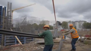 ALMATY, KAZAKHSTAN - Haziran 04 2024: Erkek işçiler vinçle kaldırmak için kayışları kaldırmak üzere ağır metal parçaları takarlar. Çağdaş inşaat alanında ekipman kaldırma kullanımı