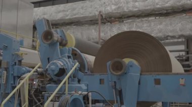 Karton kağıtların büyük kesme makinesinde rulo haline getirilmesi. Sürücü mili çekirdek hareketini yapar ve gerilim sistemi ağ germeye başlar