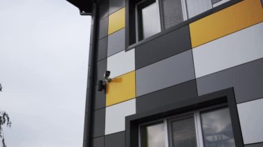 Bina duvarı parlak renkli fayanslarla kaplanmış ve pencereler bulutlu gökyüzünü yansıtmış. Binanın güvenliğine ilişkin güvenlik kameraları tarafından tamamlanan duvar