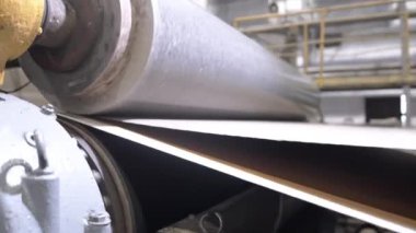 Hareket eden karton ağın yüzeyini düzleştirmek için bir makine. Büyük silindirik silindirler malzemeye dokunur, fabrika atölyesinde pürüzsüz ürün yaratır.