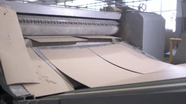 Fabrika atölyesinde büyük bir karton levha seviyelendirme makinesi. Uzun silindirik silindirler malzeme yüzeyini işleyip pürüzsüz ürün yaratıyor